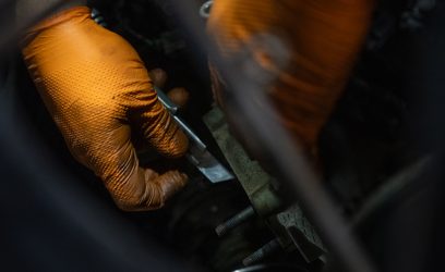 Två händer med orange handskar som mekar med en bil hos Hedemora Däck och Bilservice