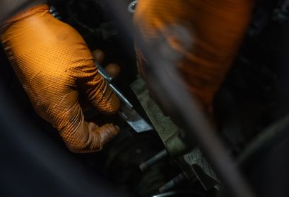 Två händer med orange handskar som mekar med en bil hos Hedemora Däck och Bilservice