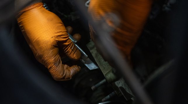 Två händer med orange handskar som mekar med en bil hos Hedemora Däck och Bilservice