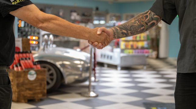 Två personer skakar hand i en butikslokal med rutigt golv.