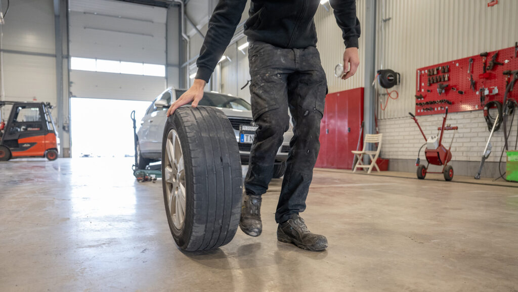 Däckverkstad i Hedemora där en man rullar ett bildäck över ett blankt golv.